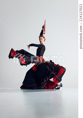 Artistry and passion. Beautiful woman, flamenco dancer with colorful fan performing traditional Spanish dance against grey studio background Artistry and passion. Beautiful woman, flamenco dancer with colorful fan performing traditional Spanish dance against grey studio background 114127021