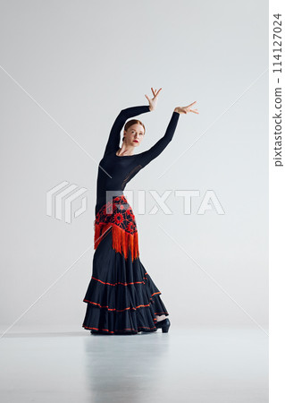 Elegant and intense performance. Tender woman dancing flamenco against grey studio background. Visual symphony of movement and color Elegant and intense performance. Tender woman dancing flamenco against grey studio background. Visual symphony of movement and color 114127024