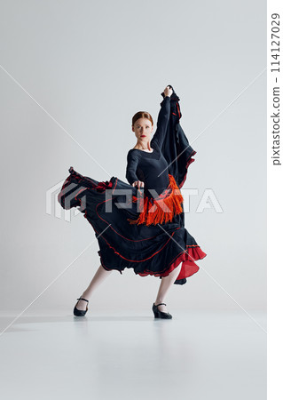 Spectacular performance of flamenco dance with elegant woman in red and black dress dancing with passion against grey studio background 114127029
