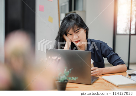 Contemplative businesswoman with a thoughtful expression working on her laptop at a desk with notes and a coffee cup. Contemplative businesswoman with a thoughtful expression working on her laptop at a desk with notes and a coffee cup. 114127033
