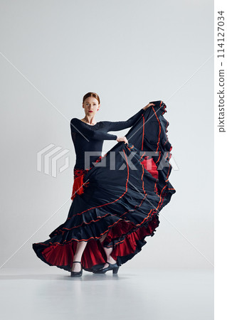 Dynamic and artistic movements. Elegant woman in traditional dress performing flamenco dance with passion against grey studio background 114127034