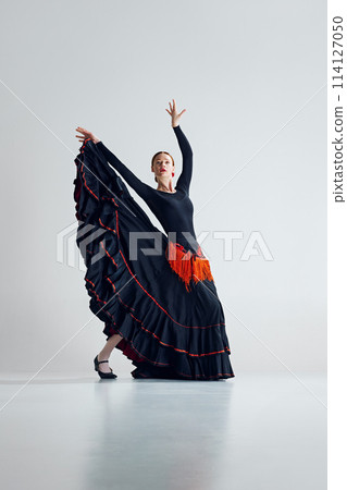 Grace of flamenco dance. Artistic talented woman in stylish dress performing flamenco against grey studio background 114127050