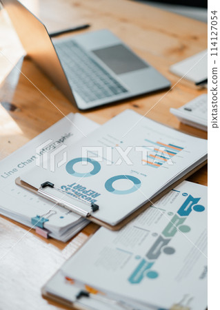 Neat and organized work desk showcasing a laptop, business infographics, and stationery, indicating a productive and data-driven environment. Neat and organized work desk showcasing a laptop, business infographics, and stationery, indicating a productive and data-driven environment. 114127054