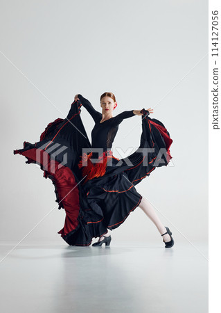 Passion and elegance. Beautiful woman in traditional dress performing flamenco dance, demonstrating artistry against grey studio background Passion and elegance. Beautiful woman in traditional dress performing flamenco dance, demonstrating artistry against grey studio background 114127056