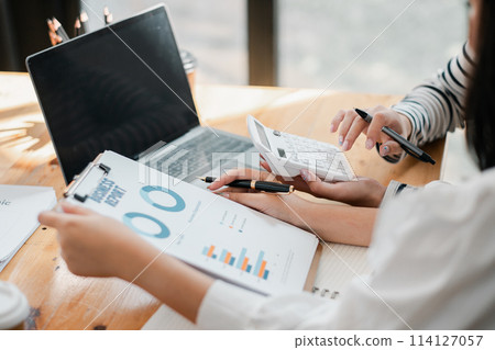 Hands of a professional analyzing financial charts and data with a calculator, accompanied by a laptop on a wooden table. Hands of a professional analyzing financial charts and data with a calculator, accompanied by a laptop on a wooden table. 114127057
