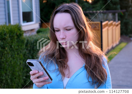 A beautiful girl in hoodie takes a selfie on her phone, pulls out her lips outdoors private sector in the city of Canada sunset backlight from behind A beautiful girl in hoodie takes a selfie on her phone, pulls out her lips outdoors private sector in the city of Canada sunset backlight from behind 114127708