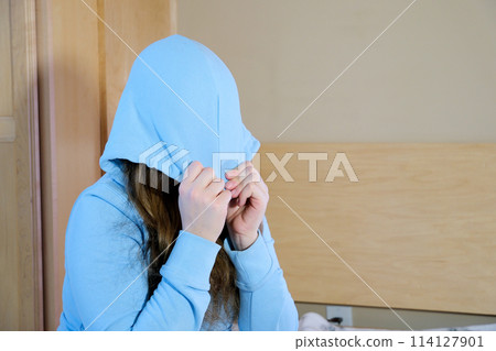 protest teenager girl teenager put a hood on her face pull a hood over her eyes in a room in the bedroom sitting alone sad crying suffering psychological problems of a child in adolescence 114127901