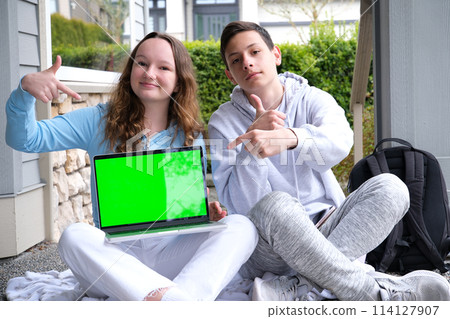people, education, technology and school concept happy students with laptop computer chromakey laptop sit on porch point finger teen boy teen girl 114127907
