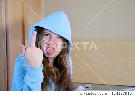 Young latin woman girl teenager hood on head stuck out tongue twisted face anger showing middle finger doing fuck you bad expression, provocation and rude attitude. screaming excited  114127910