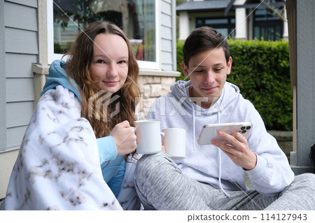 Teen boy with down syndrome pointing at laptop near friend with cup and cellphone two teenagers sit under a white blanket, boys, girls, drink tea, coffee on the porch, watch videos on a smartphone Teen boy with down syndrome pointing at laptop near friend with cup and cellphone two teenagers sit under a white blanket, boys, girls, drink tea, coffee on the porch, watch videos on a smartphone 114127943