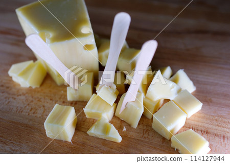 Female hands cutting cheese with a knife on a wooden cutting board. 114127944