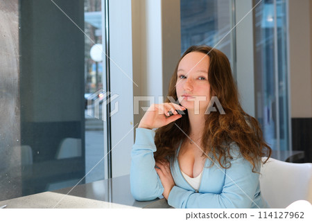 a young schoolgirl teenager sitting by the window in the classroom studying offline school institute white classroom large windows blue blouse loose hair a young schoolgirl teenager sitting by the window in the classroom studying offline school institute white classroom large windows blue blouse loose hair 114127962