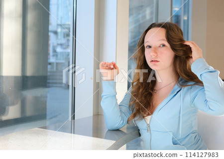 young woman straightening hair waiting for friends at school in a restaurant large white office training online internship development model school clean white face freckles there is space for text young woman straightening hair waiting for friends at school in a restaurant large white office training online internship development model school clean white face freckles there is space for text 114127983