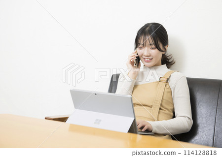 一位女士一邊使用筆記本電腦一邊打電話 114128818