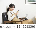 A woman checking her smartphone while using a laptop 114128890