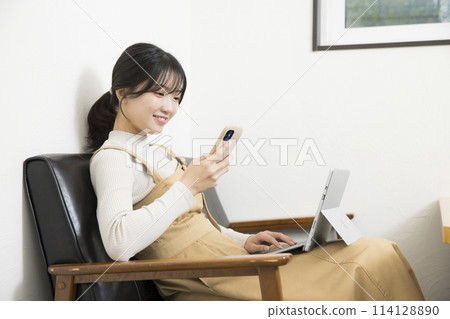 一位女士在使用筆記型電腦時檢查智慧型手機 一位女士在使用筆記型電腦時檢查智慧型手機 114128890