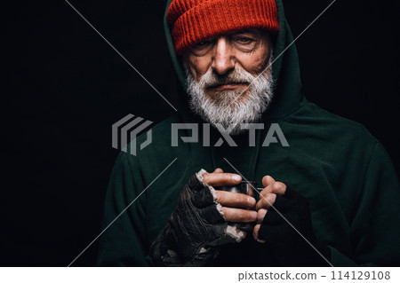 Elderly beggar being frozen outside, drinking hot water to get warm. Homeless. 114129108