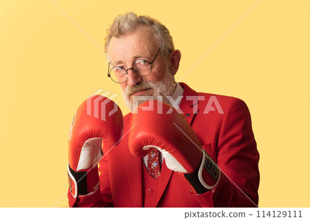 Senior business man in red suit and red boxing gloves standing in defence pose 114129111