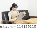 Young woman sitting on sofa and using tablet 114129115