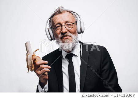 Senior businessman eats fruit while listening music in headphones during lunch 114129307