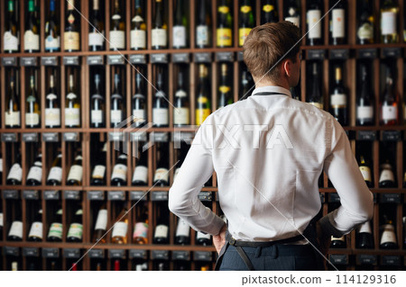 Backside of elegant wine seller selecting wine for customers in wine shop 114129316