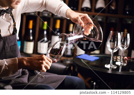 Expert decanting and pouring wine into glass. Staff training for sommelier Expert decanting and pouring wine into glass. Staff training for sommelier 114129805