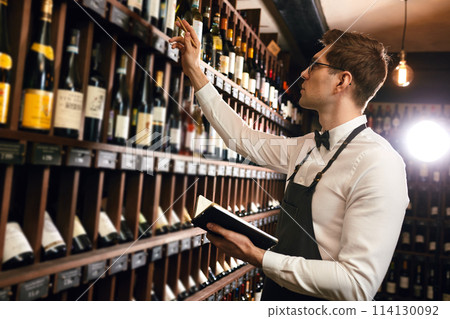 Sommelier writes at notes, putting down information on wine products in cellar Sommelier writes at notes, putting down information on wine products in cellar 114130092
