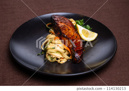 Grilled salmon with lemon and vegetables on a black plate 114130213