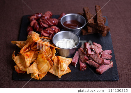 Top view of a plate of food with bread, meat, sausage, and chips with dip. 114130215