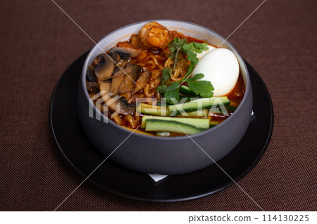 Bowl of spicy Korean ramen with mushrooms, egg, cucumber, and cilantro. 114130225