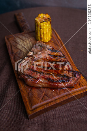 Grilled steak with corn on a wooden cutting board on brown background 114130228