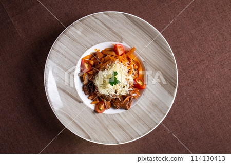 Top view of a delicious plate of beef stew with pasta, tomatoes, and cheese topping, perfect for luncha or dinner. 114130413