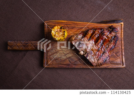 A juicy and tender grilled steak with a side of corn on the cob, served on a rustic wooden cutting board. 114130425