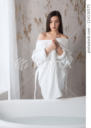 Beautiful young woman posing in bathrobe before taking bath Beautiful young woman posing in bathrobe before taking bath 114130575