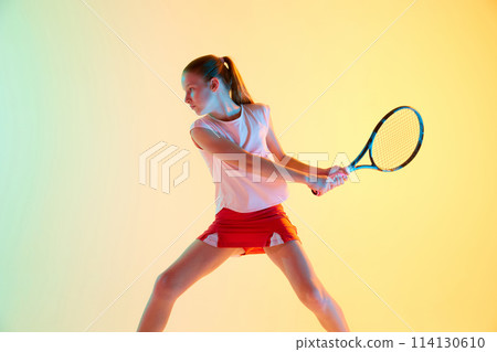 Dynamic portrait of sportive teen girl, tennis player in sports uniform training in action in neon light against blue-yellow background. Dynamic portrait of sportive teen girl, tennis player in sports uniform training in action in neon light against blue-yellow background. 114130610