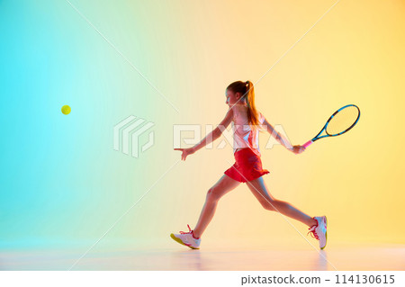 Dynamic shot of teenage girl, tennis athlete training solid cross-court forehand technique in neon light against blue-yellow background. Dynamic shot of teenage girl, tennis athlete training solid cross-court forehand technique in neon light against blue-yellow background. 114130615