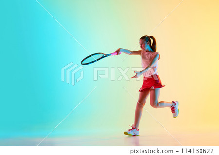 Competitive young girl, female athlete training passing shot in motion in neon light against blue-yellow background. Competitive young girl, female athlete training passing shot in motion in neon light against blue-yellow background. 114130622