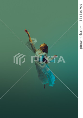 Reach for light. Woman in flowing white vintage gown reaches upwards to sky from dark teal depth of ocean waters. 114130705
