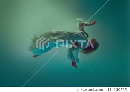 Woman dressed in white dress floating effortlessly in deep water environment that casts mystical glow of ocean. Woman dressed in white dress floating effortlessly in deep water environment that casts mystical glow of ocean. 114130735