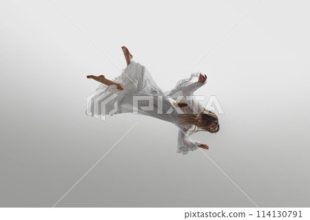 Woman dressed in vintage white gown suspend in mid-air, her long blonde hair cascading around her against white studio background. 114130791