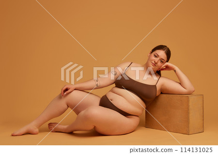 Equal beauty standards. Beautiful young girl with plus size body, wearing cotton underwear, posing against light brown studio background Equal beauty standards. Beautiful young girl with plus size body, wearing cotton underwear, posing against light brown studio background 114131025
