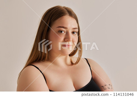 Portrait of beautiful cubby girl looking at camera against grey studio background. Unique beauty through self-care and positivity 114131046