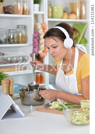 Portrait of beautiful young woman making salad and listening to music 114131961