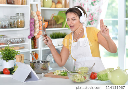 Portrait of beautiful young woman making salad and listening to music Portrait of beautiful young woman making salad and listening to music 114131967