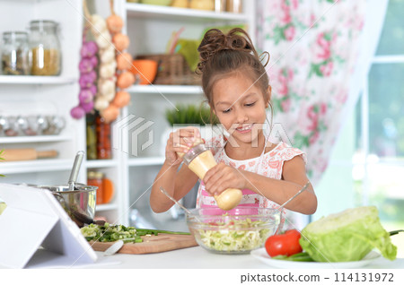 Little girl in a pink apron is making a salad. 114131972