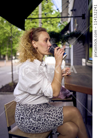 a beautiful middle age woman in 70s, 80s style clothes drinks coffee sitting at the bar in a modern cafe 114132241
