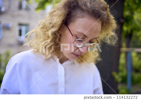 middle age woman in 70s, 80s style clothes with a coffee stain on her blouse in front of gray houses of the 70s 114132272