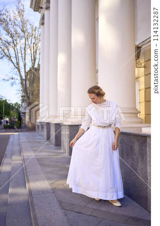 elegant middle age woman in white vintage dress near theater with antique colonnades 114132287