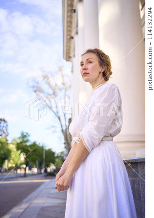 elegant middle age woman in white vintage dress near theater with antique colonnades 114132294
