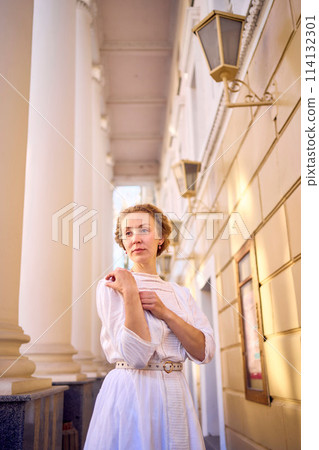 elegant middle age woman in white vintage dress near theater with antique colonnades 114132301